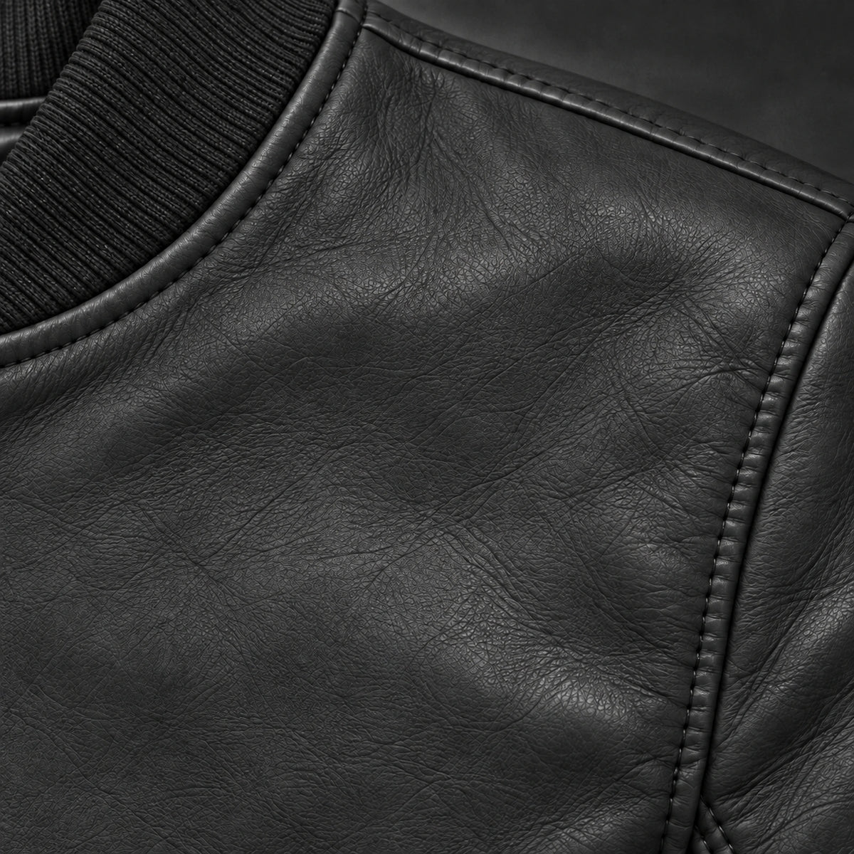 Close-up of black bomber jacket leather grain and seam stitching