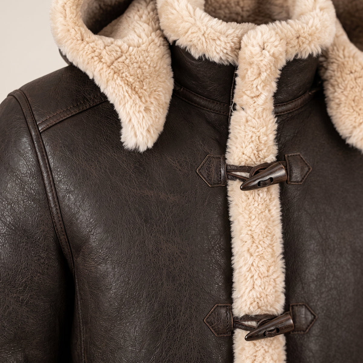 Close-up of the Wycliffe men's brown hooded shearling duffle coat showing dark brown leather, cream shearling trim and toggle fastenings.